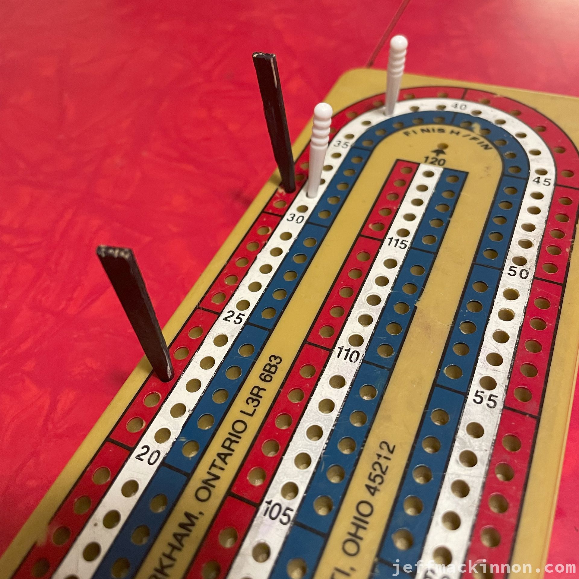 cribbage board with pegs showing the game status. White is winning over red.