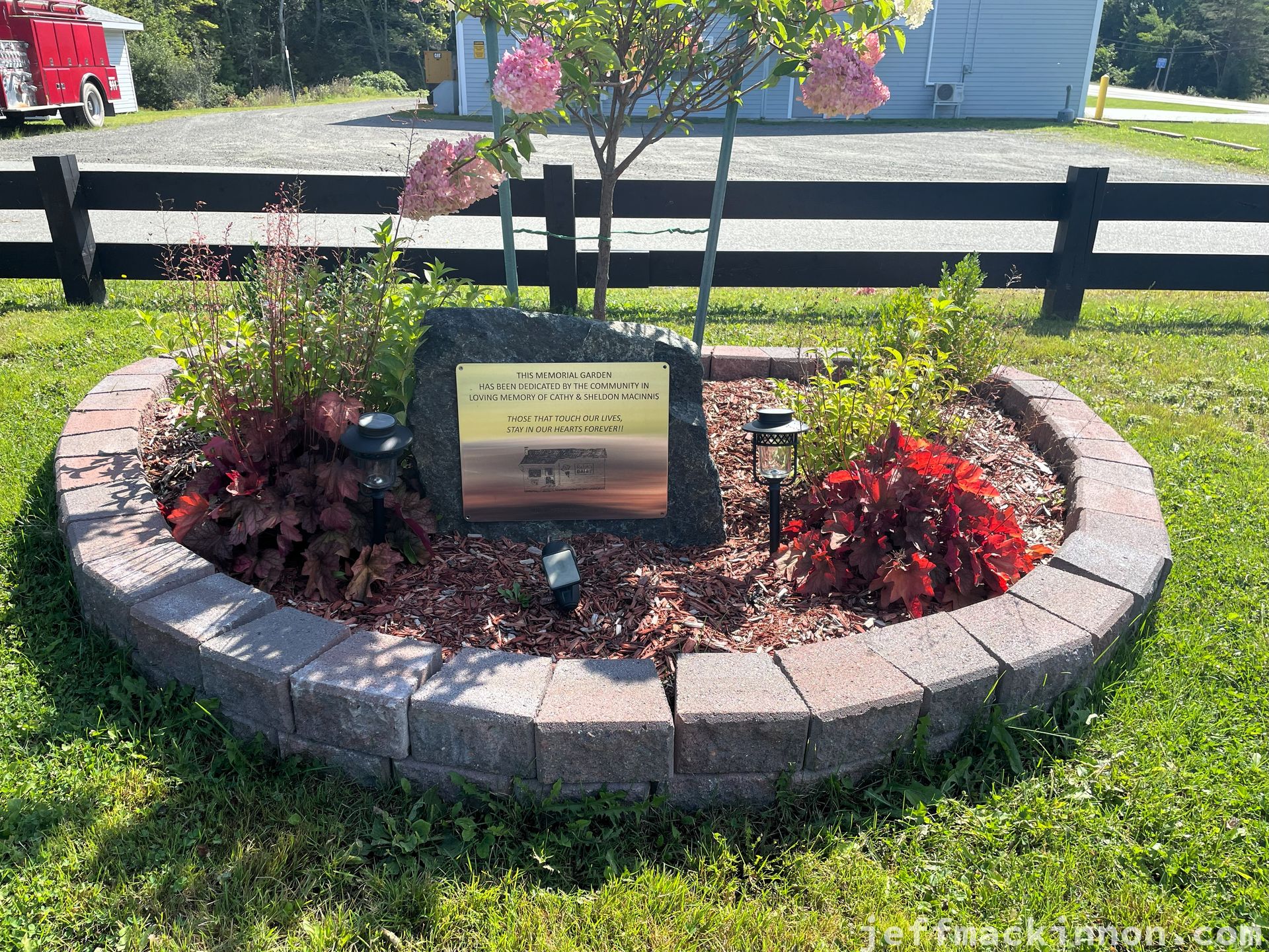 A small garden with a plaque reading, "This memorial garden has been dedicated by the community in the loving memory of Cathy and Sheldon MacInnis. *Those that touch our lives stay in our hearts forever!!*"